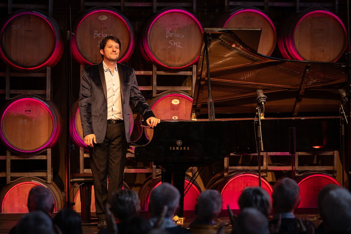 Pianist Michael Lerace acknowledges applause next to a grand piano at Coriole Music Festival 2026 in front of stacked wine barrels.